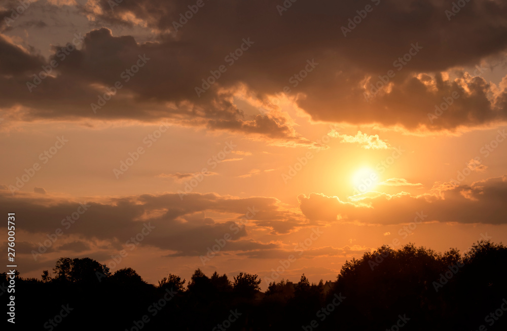 Calm evening landscape at sunset with soft air clouds, through which the rays of the setting sun