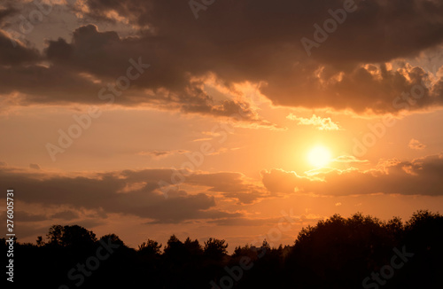 Calm evening landscape at sunset with soft air clouds, through which the rays of the setting sun