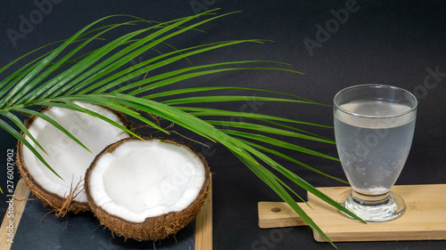 Coconut exotic fruit, two halves of the fruit in the shell, a dark background, a glass of coconut water on the kitchen and blackboard, palm palm tree, selective focus