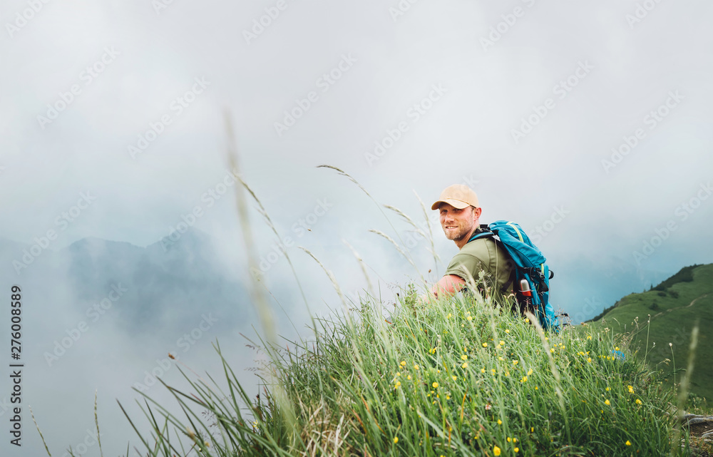 Happy backpacker man has a rest break enjoying cloudy valley bottom walking by the foggy cloudy weather mountain range . Active sports backpacking healthy lifestyle concept. Happy backpacker man has a rest break enjoying cloudy valley bottom walking by the foggy cloudy weather mountain range . Active sports backpacking healthy lifestyle concept.