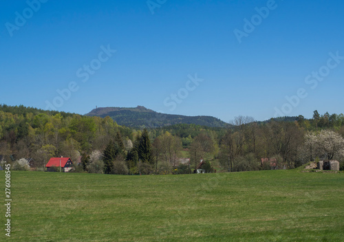 Spring landscape with view on village Marenice in Lusitian mountains with traditional wooden cottage and lush green grass meadow, birch deciduous and spruce tree forest and hills, blue sky background photo