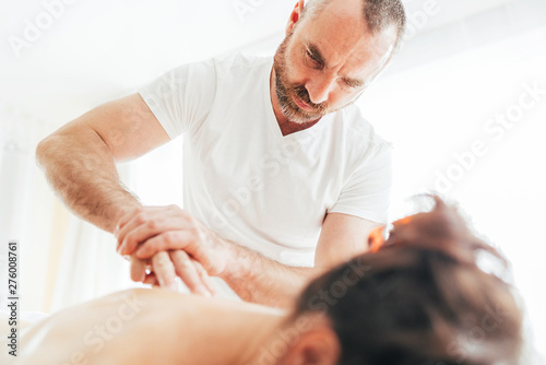 Bearded Masseur man doing massage manipulations on the Scapula area zone during young female body massaging. photo