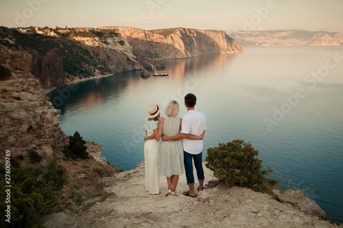 Happy family, mom, dad and daughter on the edge of the earth, overlooking the sea. People hug.