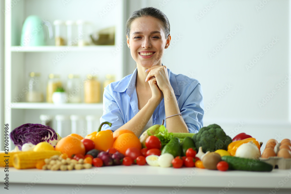 Young and cute woman sitting at the table full of fruits and vegetables in the wooden interior. Young and cute woman sitting at the table full of fruits and vegetables in the wooden interior.