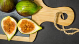 Green figs, one fruit is cut into two halves, and two whole on the wooden board with wooden handle, dark background, view from the top