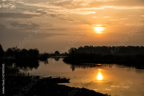 Canoes on the background of the rising sun. Landscape of the fishing village. The sun reflected in the water in the morning. Svalovychi village. Polesie. Ukraine
