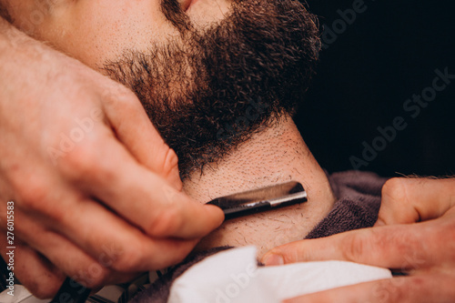 Work in the Barber shop. Barber shaving a bearded man in a barber shop, close-up. Master cuts hair and beard