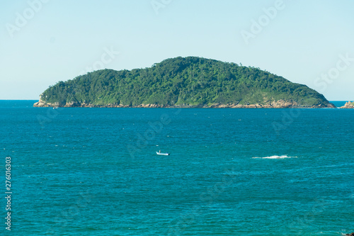 Vista do alto de um rochedo para o mar e uma ilha deserta florestada ao horizonte.