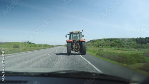 In a car following an old tractor driving on a road, Then driving past it.Two other cars in shot also driving. Driving in green nature.