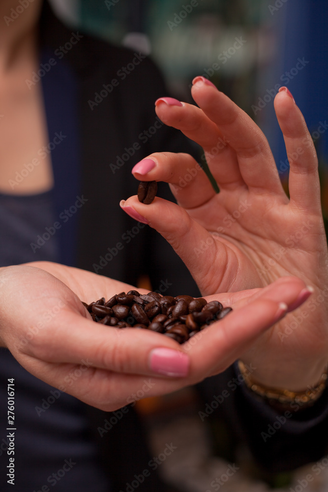Close-up of girl's hands showing roasted coffee bean with blurred background behind. Shallow depth of field focused on coffee bean. Concept of individual approach to quality control. Close-up of girl's hands showing roasted coffee bean with blurred background behind. Shallow depth of field focused on coffee bean. Concept of individual approach to quality control.