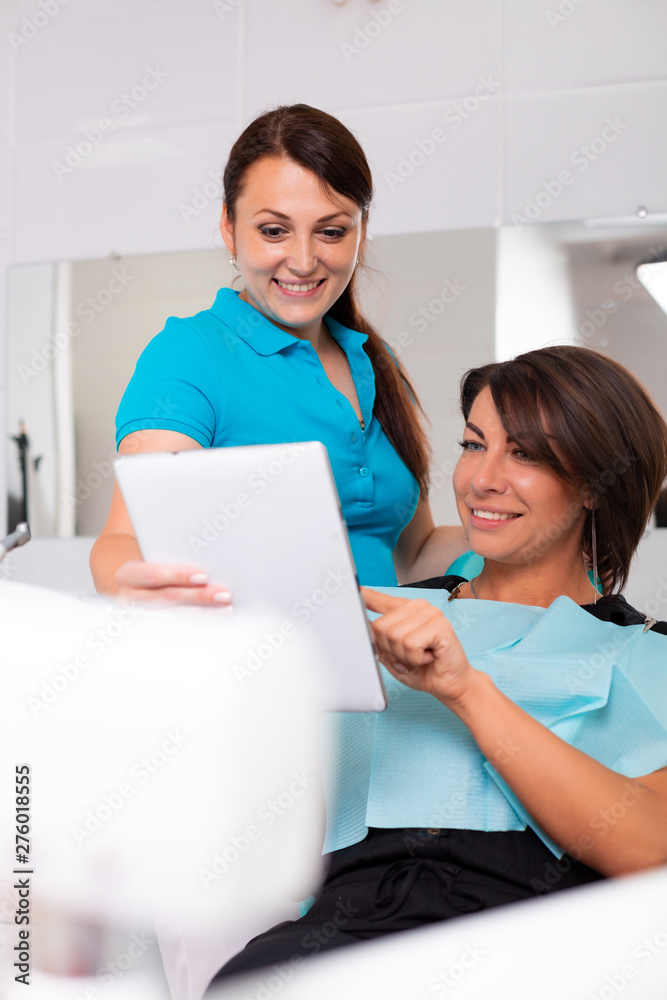 Female dentist showing teeth x-ray on digital tablet screen. Patient sitting on chair in professional dental clinic Female dentist showing teeth x-ray on digital tablet screen. Patient sitting on chair in professional dental clinic