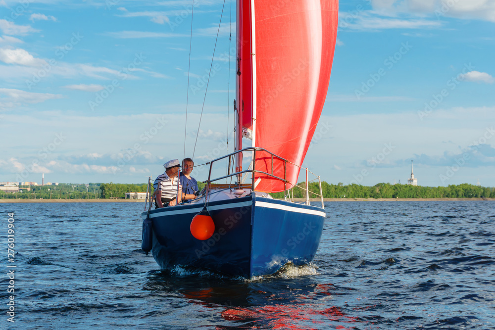 Fototapeta premium sailboat with red sails on the background of the shore with an urban landscape