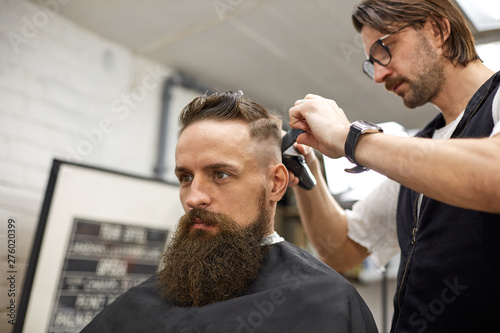 Brutal guy in modern Barber Shop. Hairdresser makes hairstyle a man with a long beard. Master hairdresser does hairstyle with hair clipper