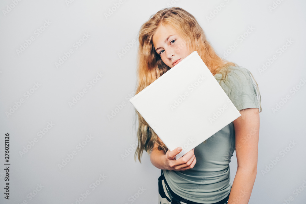 Caucasian girl and square mockup poster. Copy space. Beautiful teen girl holding in her hand blank canvas and standing over grey background. Caucasian girl and square mockup poster. Copy space. Beautiful teen girl holding in her hand blank canvas and standing over grey background.