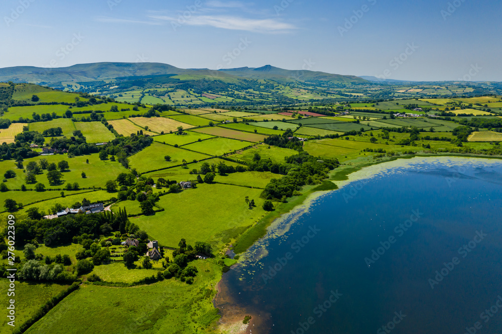 Aerial drone view of a lake surrounded by green farmland and fields in rural Wales (Llangorse Lake)