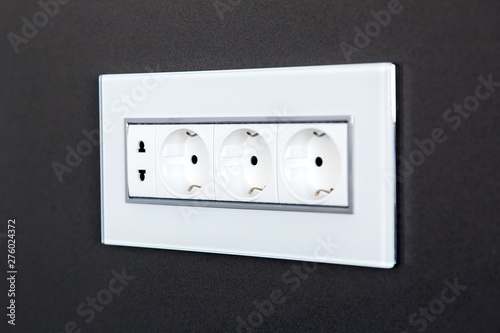 socket with plugs for standard type A plug and standard type F plug in white plastic case on a dark gray stone wall, close up side view.