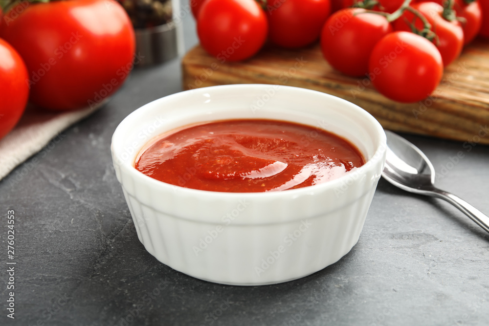 Composition with bowl of tomato sauce on grey table Composition with bowl of tomato sauce on grey table
