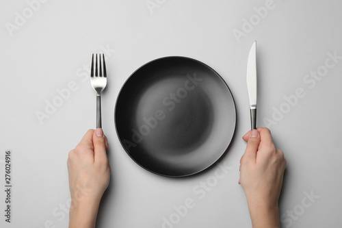 Woman with fork, knife and empty plate on grey background, top view