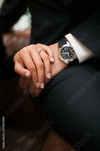 Concept of wrist watch advertising. Close up of holding hands. Elegant man in a black suit and Rich woman in black dress. Young Fashion stylish man and woman in loft design interior.
