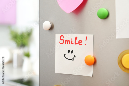 Note with word "Smile" and colorful magnets on refrigerator door in kitchen. Space for text