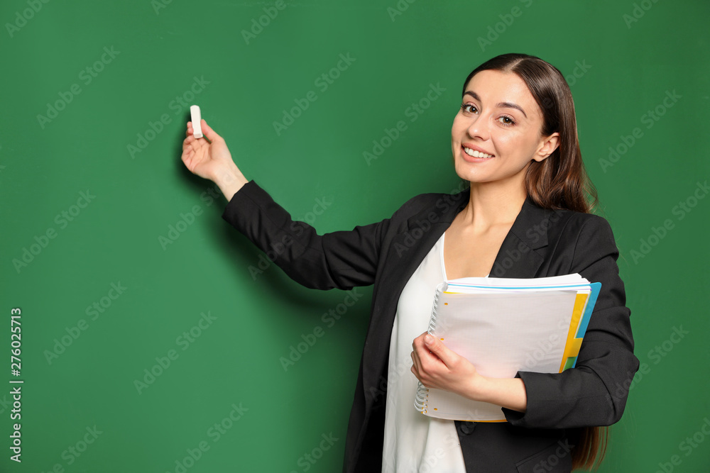 Portrait of young teacher with notebook and chalk on green background. Space for text Portrait of young teacher with notebook and chalk on green background. Space for text