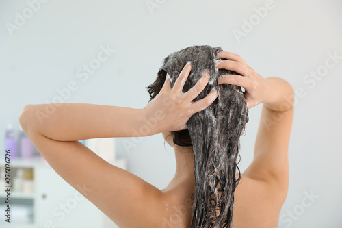 Woman applying shampoo onto her hair in light bathroom