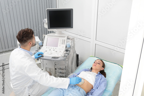 Doctor conducting ultrasound examination of patient's abdomen in clinic