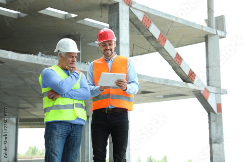 Professional engineer with tablet and foreman in safety equipment at construction site. Space for text