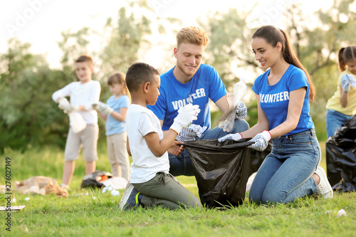 Little African-American boy collecting trash with volunteers in park
