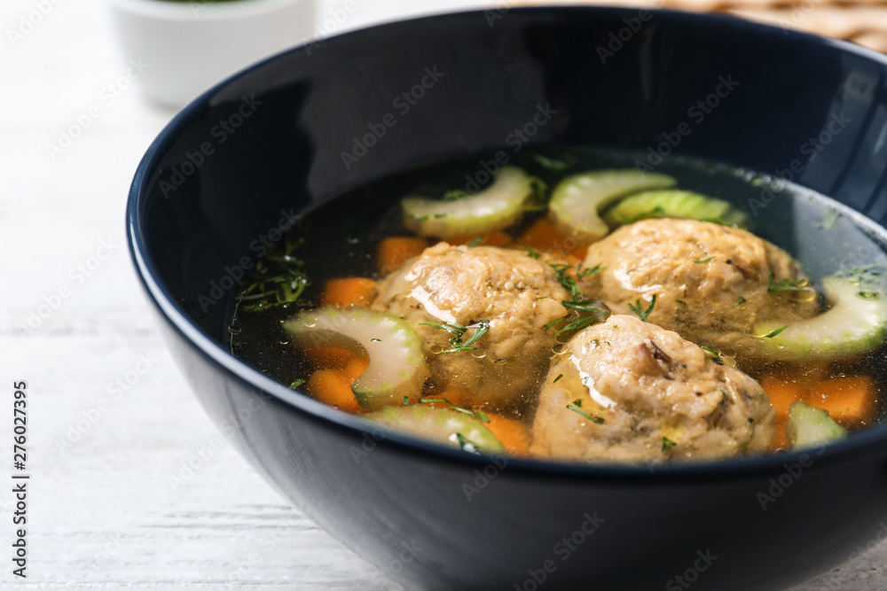 Bowl of Jewish matzoh balls soup on white wooden table, closeup