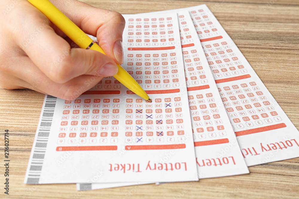 Obraz premium Woman filling out lottery tickets with pen on wooden table, closeup. Space for text