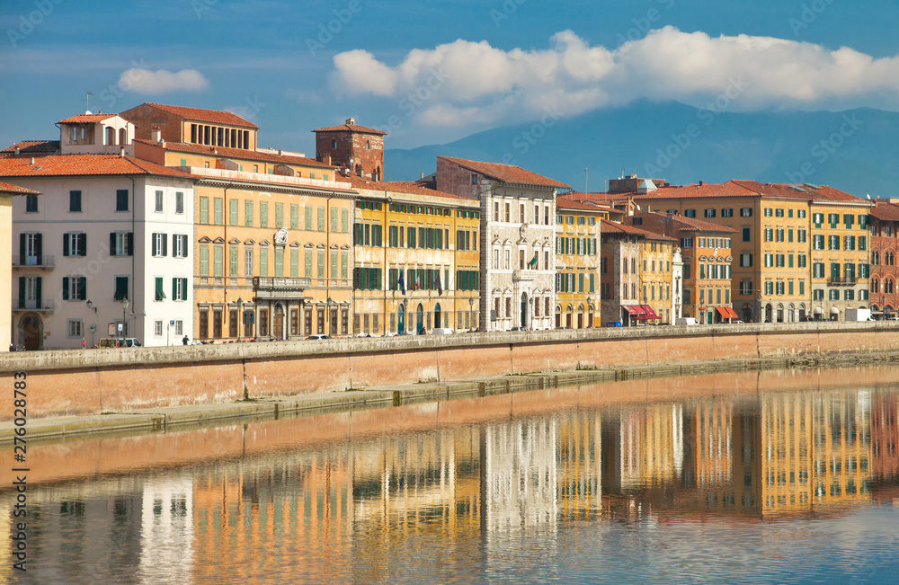 yellow facades with wooden windows with traditional green shutters of old Italian houses on the embankment of the river Arno, reflected in the water on a sunny day in the city of Pisa, Tuscany, Italy
