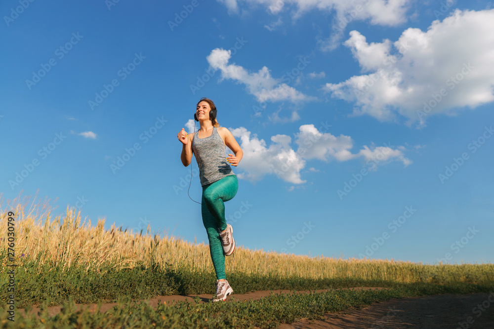 Sport, fitness, health care, cardio training. Active woman with athletic body running in the countryside. Smiling female jogger working out in the morning sunny day. Sport, fitness, health care, cardio training. Active woman with athletic body running in the countryside. Smiling female jogger working out in the morning sunny day.