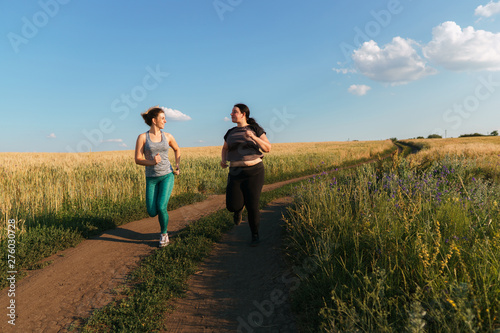 Young fit woman support and motivate her overweight female friend at outdoor jogging. Friendship, personal trainer, group workout, weight loss, sports and health care