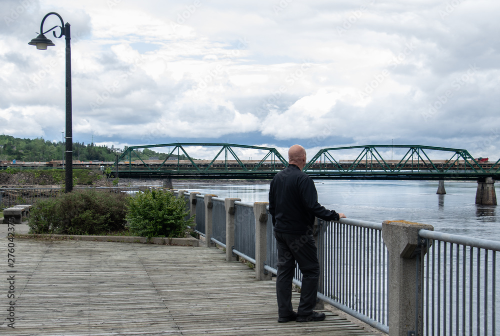 A man looks at bridge spanning the Saguenay River in from the port boardwalk in Chicoutimi Quebecc A man looks at bridge spanning the Saguenay River in from the port boardwalk in Chicoutimi Quebecc