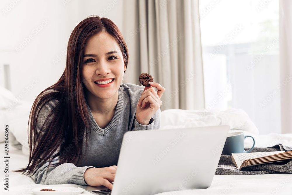 Young woman relaxing and drinking cup of hot coffee or tea using laptop computer on a cold winter day in the bedroom.woman checking social apps and working.Communication and technology concept Young woman relaxing and drinking cup of hot coffee or tea using laptop computer on a cold winter day in the bedroom.woman checking social apps and working.Communication and technology concept