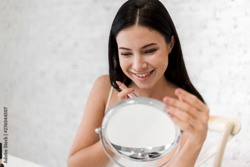 Smiling beautiful woman fresh healthy skin looking on mirror and enjoying applying lips with red lipstick at home.facial beauty and cosmetic concept Smiling beautiful woman fresh healthy skin looking on mirror and enjoying applying lips with red lipstick at home.facial beauty and cosmetic concept