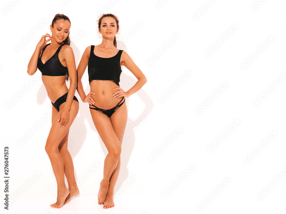 Two beautiful sexy smiling hipster women in black lingerie. Trendy hot models having fun in studio. Girls isolated on white. Full length Two beautiful sexy smiling hipster women in black lingerie. Trendy hot models having fun in studio. Girls isolated on white. Full length