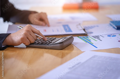 Businessman holding a pen and analyze the marketing plan with calculator on wood desk in office. Finance concept.