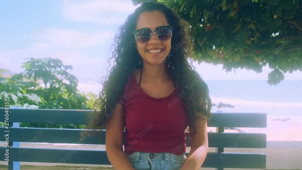 Woman siting on the bench. Beautiful young woman with curly hair smiling with the sea in the background.