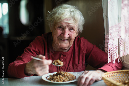 The old woman laughs at dinner at the table in the house.