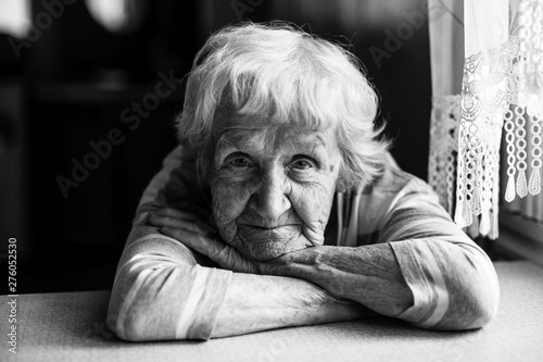 Close-up black and white portrait of a old woman at the table in home.