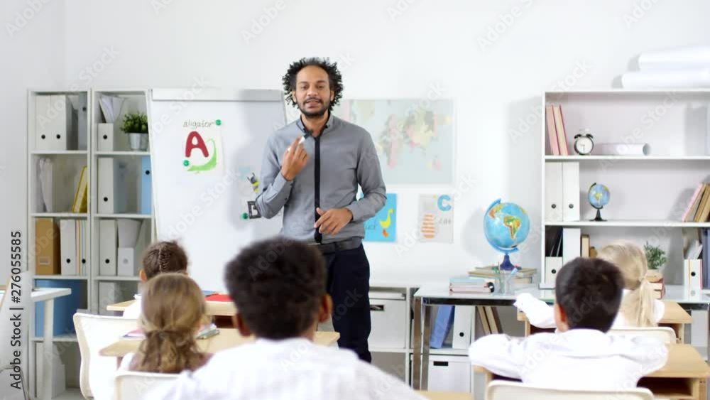 Tracking shot of male Arab preschool teacher teaching alphabet to group of little kids sitting at their desks Tracking shot of male Arab preschool teacher teaching alphabet to group of little kids sitting at their desks