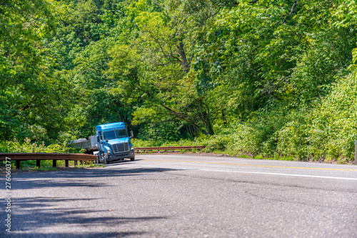 Blue big rig low cab semi truck go up the hill on the winding road in forest