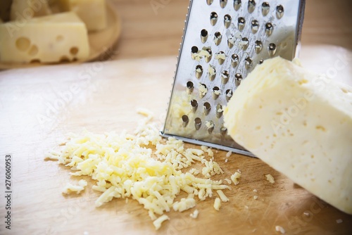 Woman preparing cheese for cook using cheese grater in the kitchen - people making food with cheese concept