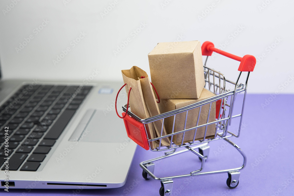 Shopping cart with purchases - packages and boxes on the modern laptop on trendy purple background. Online shopping and sale concept.