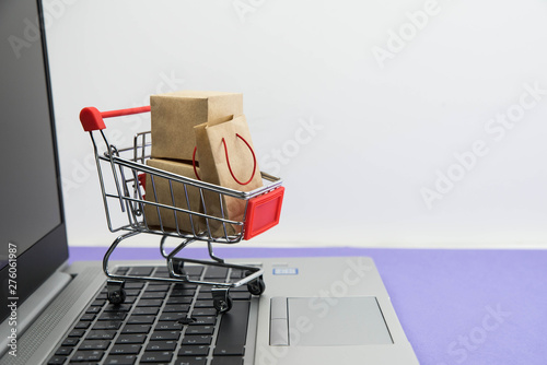 Shopping cart with purchases - packages and boxes on the modern laptop on trendy purple background. Online shopping and sale concept.
