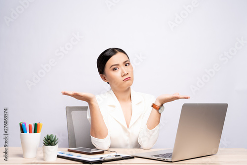Portrait of a confused woman sitting at office isolated over background photo