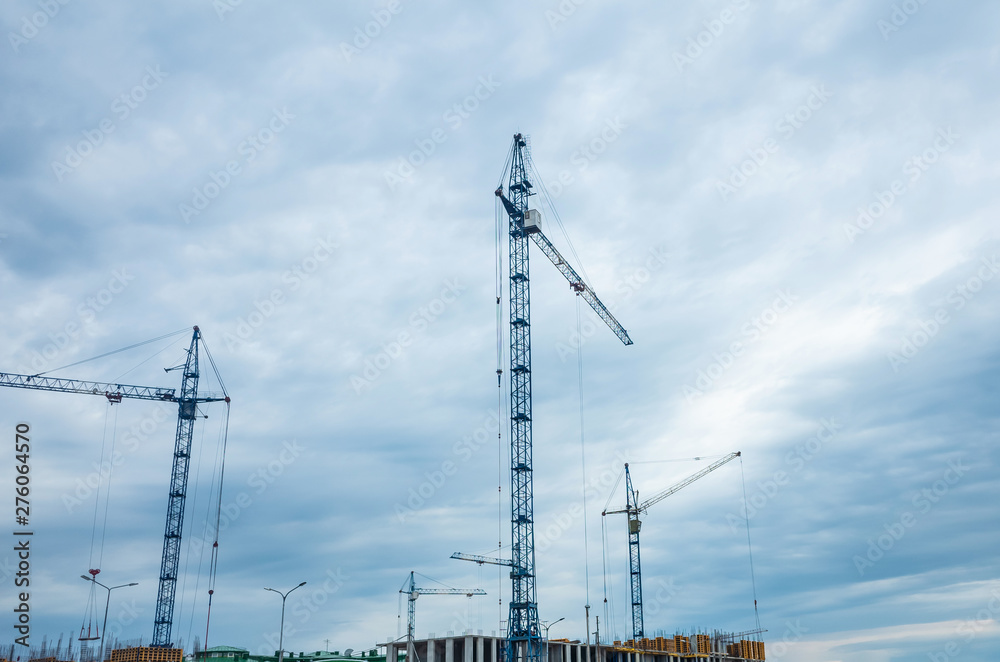 Construction cranes on a cloudy sky background. The concept of building houses, urban development. Place for text, background image. Cityscape.