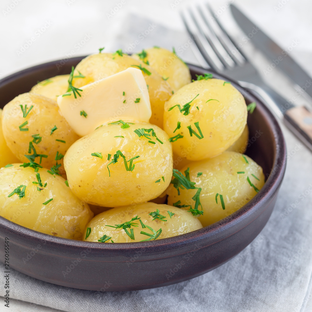 New young boiled potato topped with melted butter and chopped dill in a ceramic bowl, square format New young boiled potato topped with melted butter and chopped dill in a ceramic bowl, square format